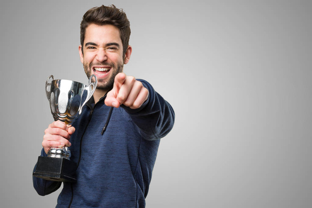 young man holding a trophy and pointing front on grey background - Photo, Image