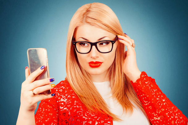 I am beautiful and I know it. Portrait of a young attractive blonde woman making selfie photo on smartphone wearing red lace jacket and white formal shirt isolated on dark blue background with copy space. - Foto, Imagem