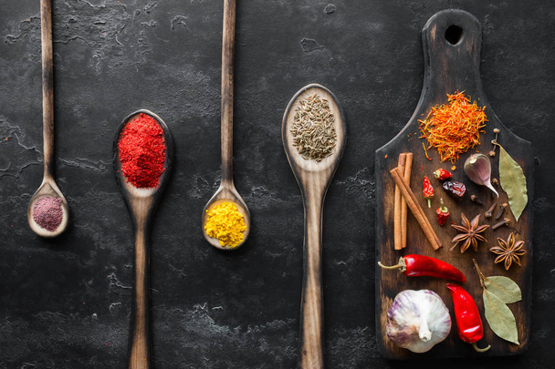 cutting board with seasonings and spoons with spices on a black background - 写真・画像