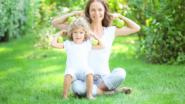 happy family sitting on green grass and playing with fruits and vegetables in spring park. healthy eating concept - Footage, Video