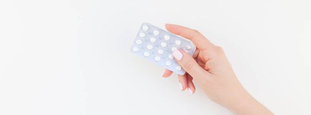 Woman hand with pastel manicure polish holding pills in blister isolated on white background with copy space. Long wide banner for feminine beauty blog social media. Female healthcare concept - Photo, Image