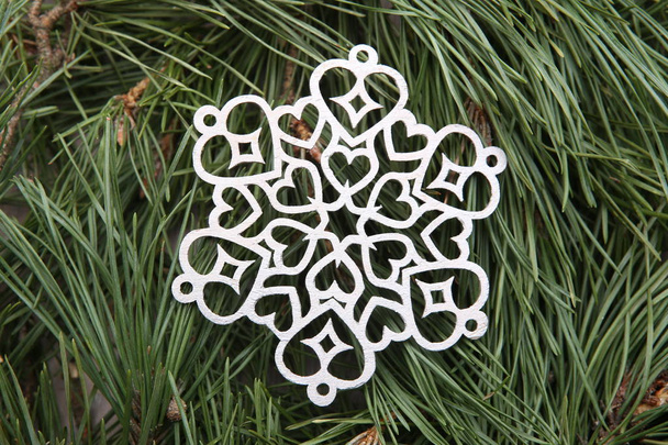 silbernes Schneeflockenornament auf grünem Kiefernzweig Hintergrund. Winter Weihnachtsdekoration Faulenzer schneiden Schneeflocke auf Tannenzweige. - Foto, Bild