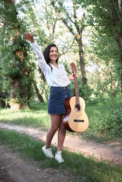 joven mujer caminando en el bosque y tocando la guitarra, la naturaleza de verano, la luz del sol brillante, sombras y hojas verdes, sentimientos románticos
 - Foto, imagen