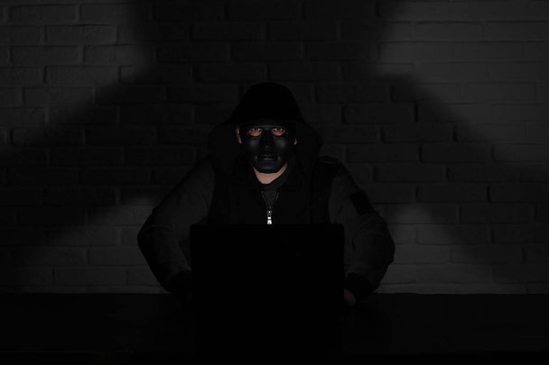 Hacker con máscara negra y capucha en la mesa
 - Foto, Imagen