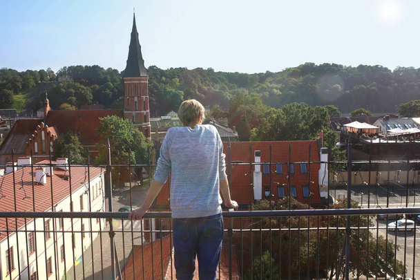 Man enjoying cityscape on roof terrace in old town. Woman looking to old town panorama of Kaunas city in Lithuania, in horizon Vytautas The Great Church. - Фото, зображення