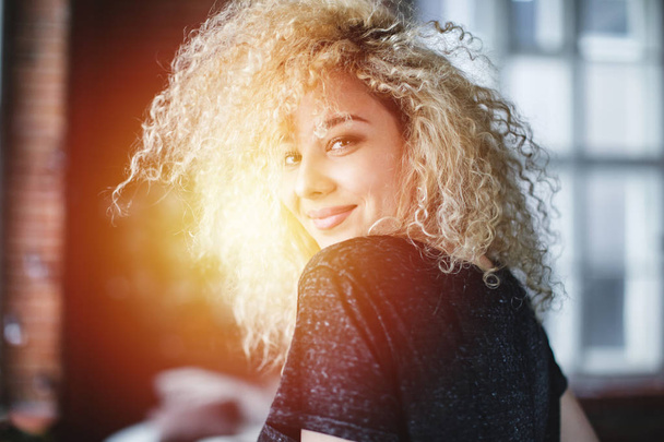 Young smiling woman with curly hair in a loft. Emotional portrait. - Foto, afbeelding