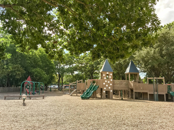 Parco giochi pubblico in legno per bambini come forte o castello con sezioni separate per diverse età. Gioca struttura set sotto il rigoglioso di alberi più grandi in Texas, Stati Uniti, foglie estive verde e cielo blu nuvola
 - Foto, immagini