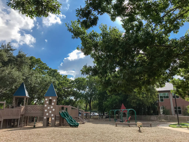 Veřejné dřevěné dětské hřiště jako pevnost nebo hrad s oddělenými částmi pro různé věkové kategorie. Play set struktury pod svěží větších stromů v Texasu, Usa, v létě listy zelené a cloud blue sky - Fotografie, Obrázek