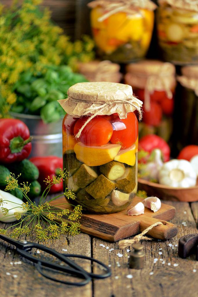 Homemade marinated assorted with tomato, cucumber and squash, dill, carrot, garlic and onion in a jar on an old wooden background. Rustic style - Photo, Image