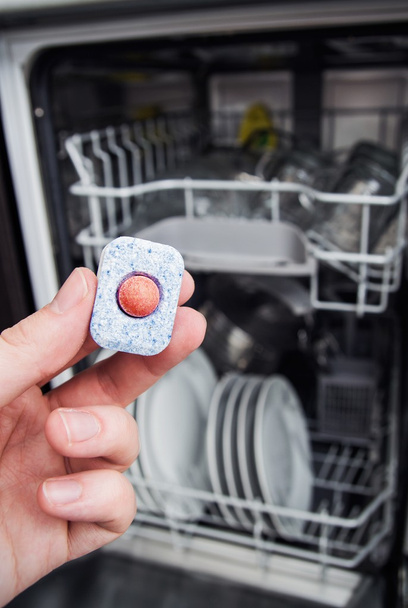 Hand holding dishwashing tablet. Dishwasher in background - Photo, image