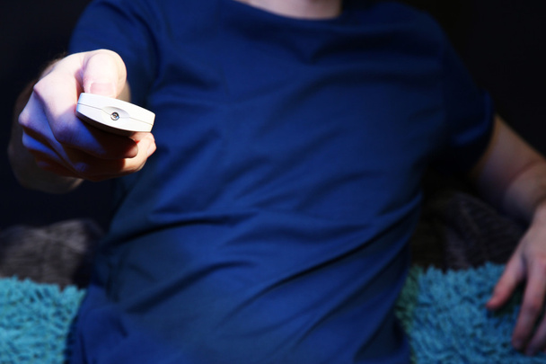 Man hand holding a TV remote control, on dark background - Fotó, kép
