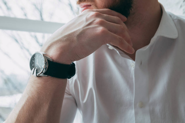 Bijgesneden beeld van de baas, is stutten zijn hand op de kin, op zijn arm een dure en stijlvol horloge, tegen de achtergrond van het venster, het concept - Foto, afbeelding