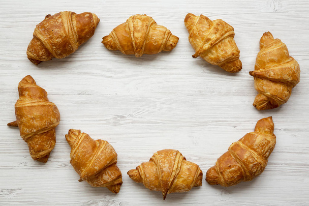 Frame of freshly baked croissants on white wooden surface, top view. From above, overhead, flat lay. Copy space. - Фото, изображение