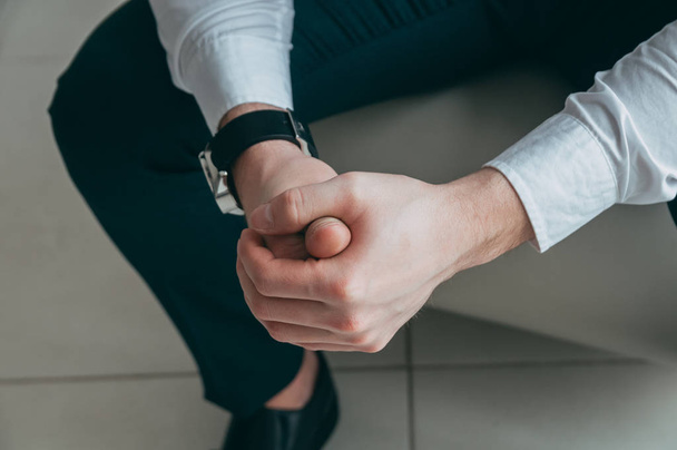 Обрізаний вид боса, що тримає руки разом, на руці дорогий і стильний годинник, на тлі ноги, вид зверху
 - Фото, зображення