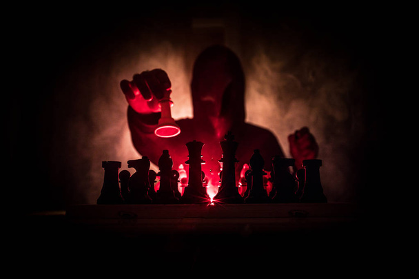 Un uomo che gioca a scacchi. Spaventosa silhouette sfocata di una persona alla scacchiera con figure scacchistiche. Sfondo scuro e nebbioso. Concentrazione selettiva. Concetto di orrore
 - Foto, immagini