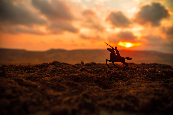 World war officer (or warrior) rider on horse with a sword ready to fight and soldiers on a dark foggy toned sunset background. Battle scene battlefield of fighting soldiers. Selective focus - Photo, Image