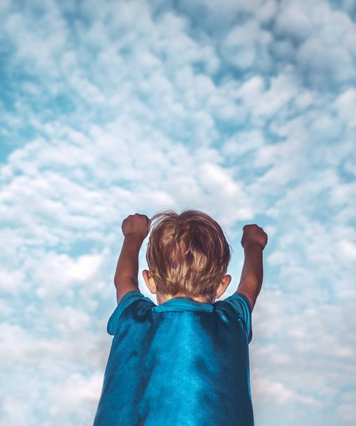 Мальчик играет в супермене, вид сзади на маленького мальчика в костюме супергероя с поднятыми руками пытается летать в небе, счастливая детская концепция
 - Фото, изображение