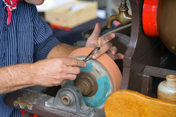 Close-up shot of a man's hands sharpening a scissors. Elderly specialist sharpening a scissors. Scissors sharpening in the workshop,workers hands. - Photo, Image
