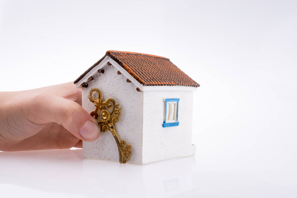 Рука держит золотой ключ рядом с домом на белом фоне - Фото, изображение
