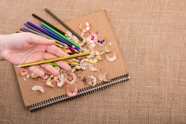 Hand hält Farbstift über ein Notizbuch mit Bleistiftspänen - Foto, Bild