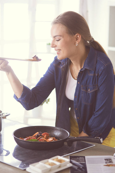Young woman cooking healthy food holding a pan with vegetables is it. Healthy lifestyle, cooking at home concept - Fotó, kép