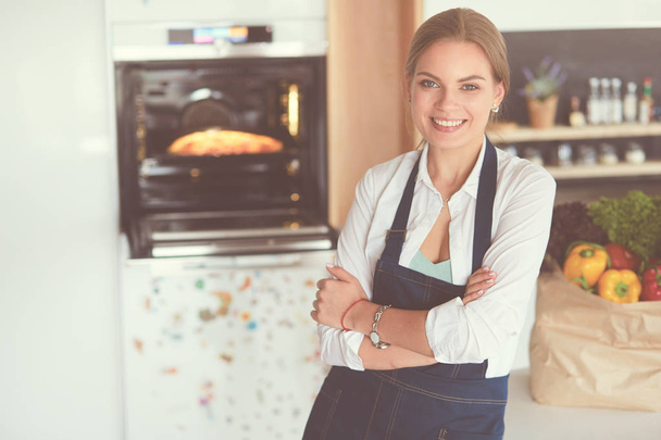 Portrait of young woman standing with arms crossed against kitchen background - Photo, Image