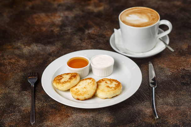 Cottage cheese curd pancakes or fritters with latte coffee on brown background - Photo, image