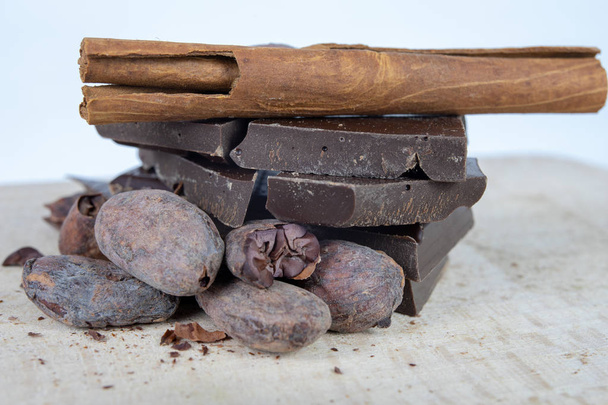 Tasty dark chocolate and cocoa beans on a white table. Sweets used to prepare desserts in the kitchen. White background. - Foto, imagen