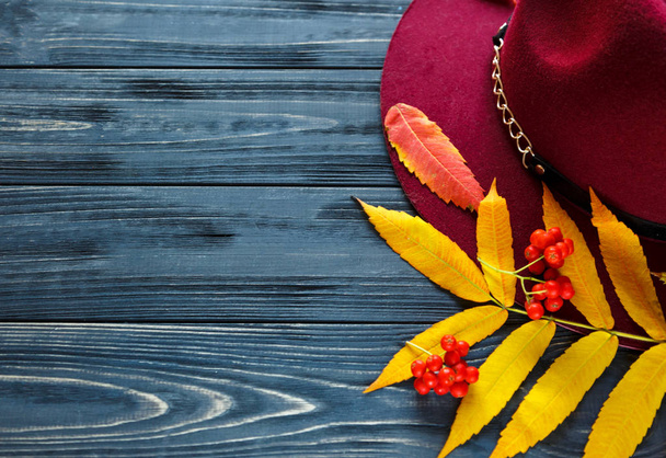  Sombrero de color burdeos sobre un fondo de madera gris con hojas de color rojo otoño, amarillo. Tendencia de moda otoño, invierno
, - Foto, imagen