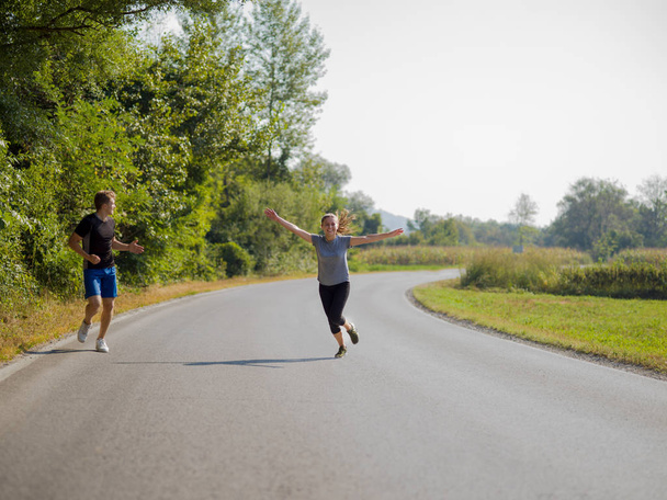 young couple enjoying in a healthy lifestyle while jogging along a country road, exercise and fitness concept - Фото, изображение