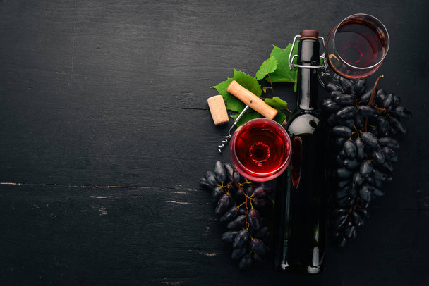 Red wine in a bottle with a glass and grapes. On a black wooden background. Free space for text. Top view. - Foto, Imagem