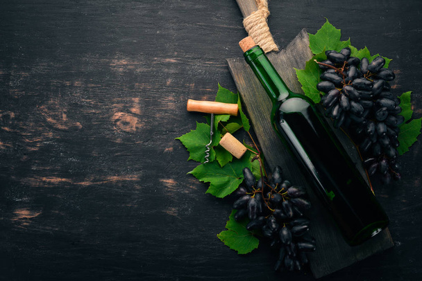 A bottle of red wine on a black wooden background. Grape. Free space for text. Top view. - Zdjęcie, obraz
