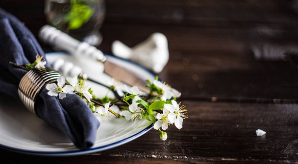 Frühling florales Konzept mit blühenden Kirschbaumzweigen und serviert mit rustikalem Geschirr auf dunklem Holztisch - Foto, Bild