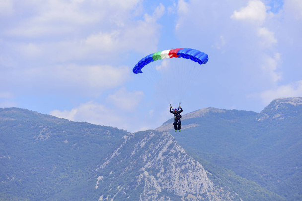 парашутист спускається на блакитне небо, на задньому плані гори
 - Фото, зображення