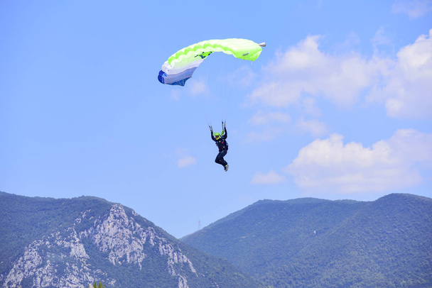 paracaidista desciende contra un cielo azul, en el fondo las montañas
 - Foto, imagen