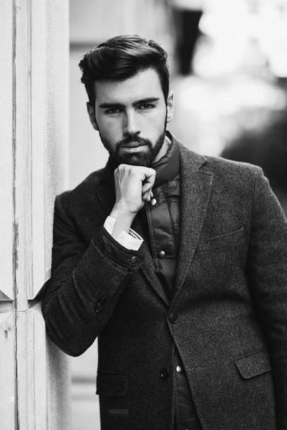 Young bearded man, model of fashion, in urban background wearing british elegant suit. Guy with beard and modern hairstyle in the street. - Photo, Image