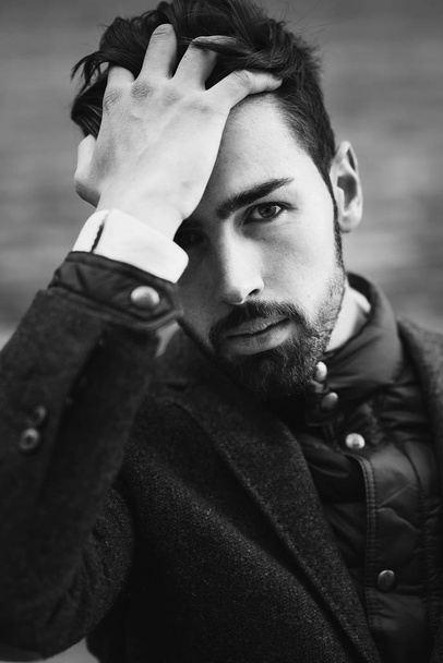 Young bearded man, model of fashion, in urban background wearing british elegant suit. Guy with beard and modern hairstyle touching his hair - Foto, Bild