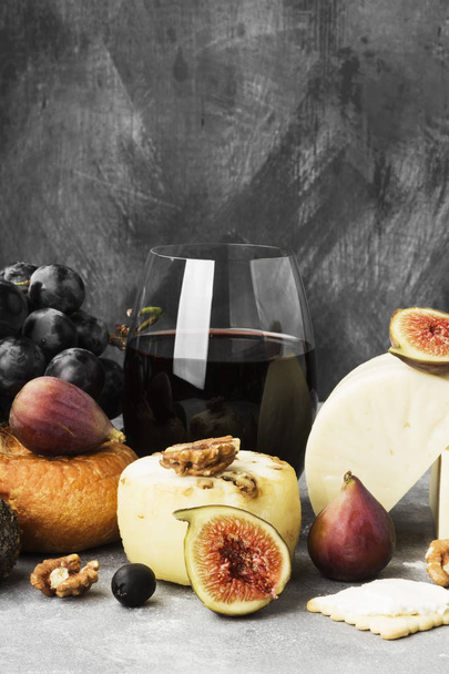 Snacks with wine - various types of cheeses, figs, nuts, honey, grapes on a gray background - 写真・画像