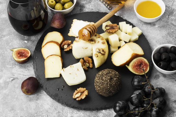Snacks with wine - various types of cheeses, figs, nuts, honey, grapes on a gray background - 写真・画像