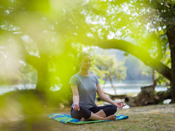 Zdravá žena uvolňující, zatímco meditaci a dělal cvičení v krásné přírodě na břehu řeky - Fotografie, Obrázek