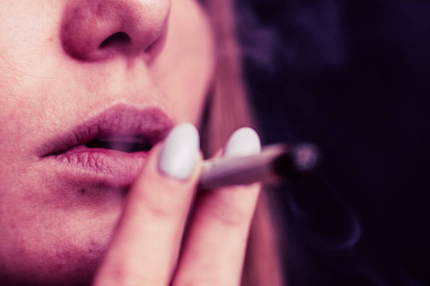 eine Frau raucht Cannabis mit einem Joint und einem Feuerzeug in seinen Händen. Rauch auf schwarzem Hintergrund. Konzepte des medizinischen Marihuanakonsums und der Legalisierung von Cannabis. auf schwarzem Hintergrund rosa Tönung - Foto, Bild