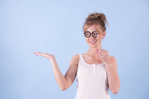 Elegant young woman pretending wearing funny nerd eyeglasses showing copy space on hand. Education and studying females look concept. - Photo, Image