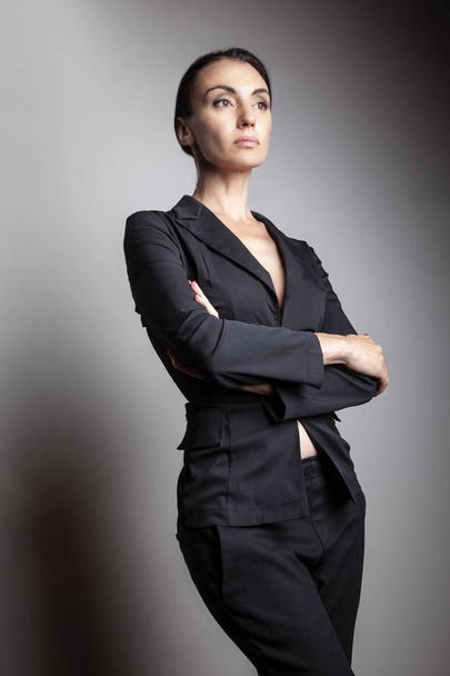 暗い背景に交差した腕を持つスーツ立ってのスタイリッシュな女性実業家  - 写真・画像