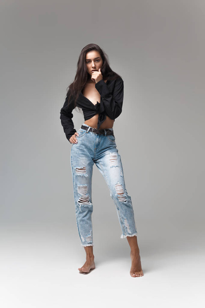 Young cool hipster girl in black shirt and blue banana jeans on gray background. Fashionable modern style - Foto, Imagem