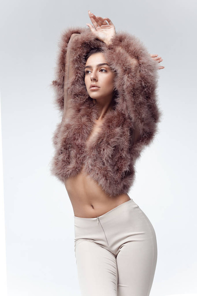 Young elegant girl posing in fluffy pink cape with artificial fur and beige flare trousers on gray background. Fashion retro style - Φωτογραφία, εικόνα