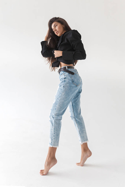 Young cool hipster girl in black shirt and blue banana jeans on white background. Fashionable modern style - Fotó, kép