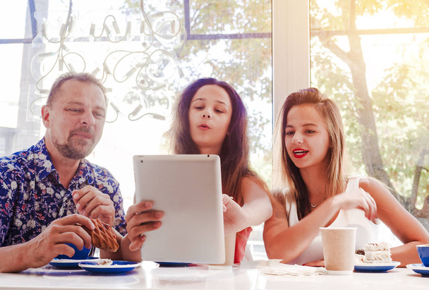 Happy family eating breakfast and using tablet. A big company with a digital tablet in cafe, smiling happy man and his children looking to the screen, using internet, buy online - Foto, imagen