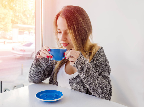 woman in a cafe drinking coffee.Fashionable girl with toned long hair feeling happy with her cup of tea - Фото, зображення