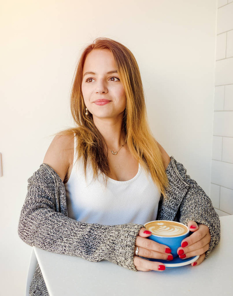 woman in a cafe drinking coffee.Fashionable girl with toned long hair feeling happy with her cup of tea - Foto, afbeelding