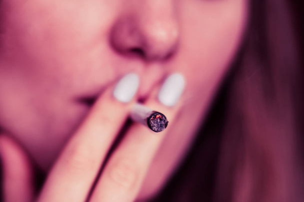 raucht Cannabiskraut, einen Joint und ein Feuerzeug in seinen Händen. Rauch auf schwarzem Hintergrund. Konzepte des medizinischen Marihuanakonsums und der Legalisierung von Cannabis. auf schwarzem Hintergrund rosa Tönung - Foto, Bild